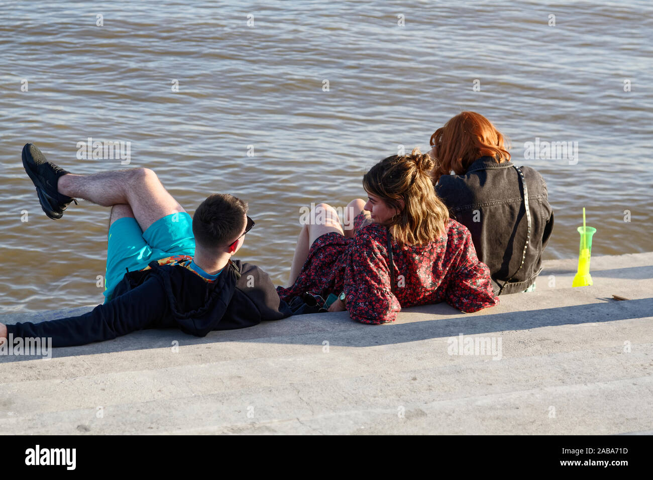 3 people sitting by water, talking, neon daiquiri glass, friends, Moonwalk; Mississippi River, New Orleans; LA; USA; autumn; horizontal Stock Photo