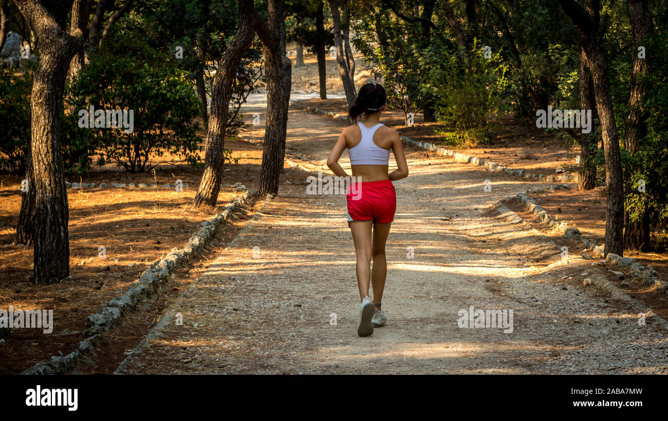 Teen in red shorts and white tanktop jogging on dirt trail from the back in Athens Greece Stock Photo