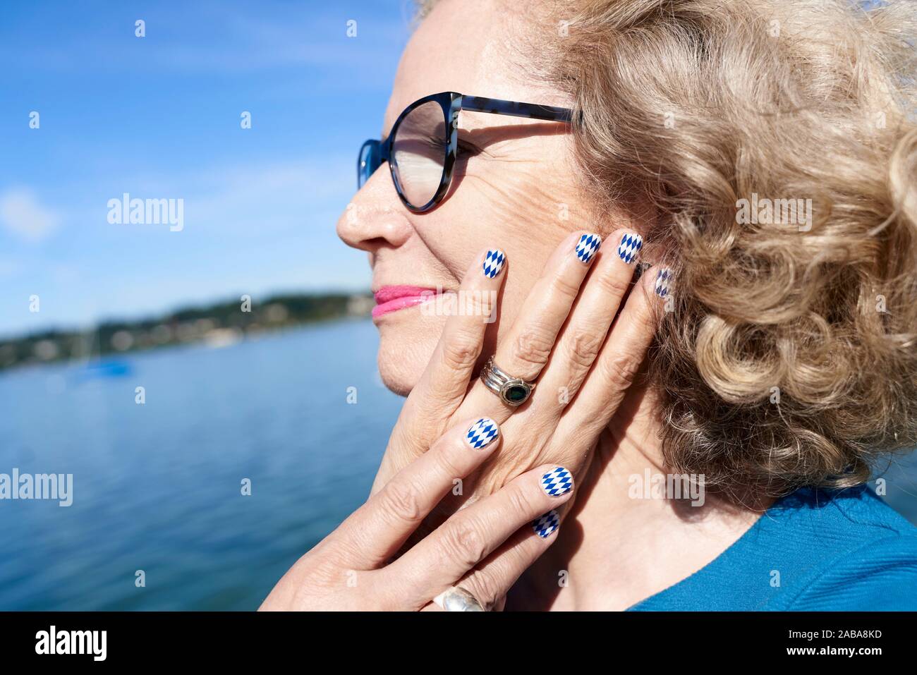 Portrait of senior woman with Bavarian flag painted on finger nails, by Lake Starnberg. Bavaria