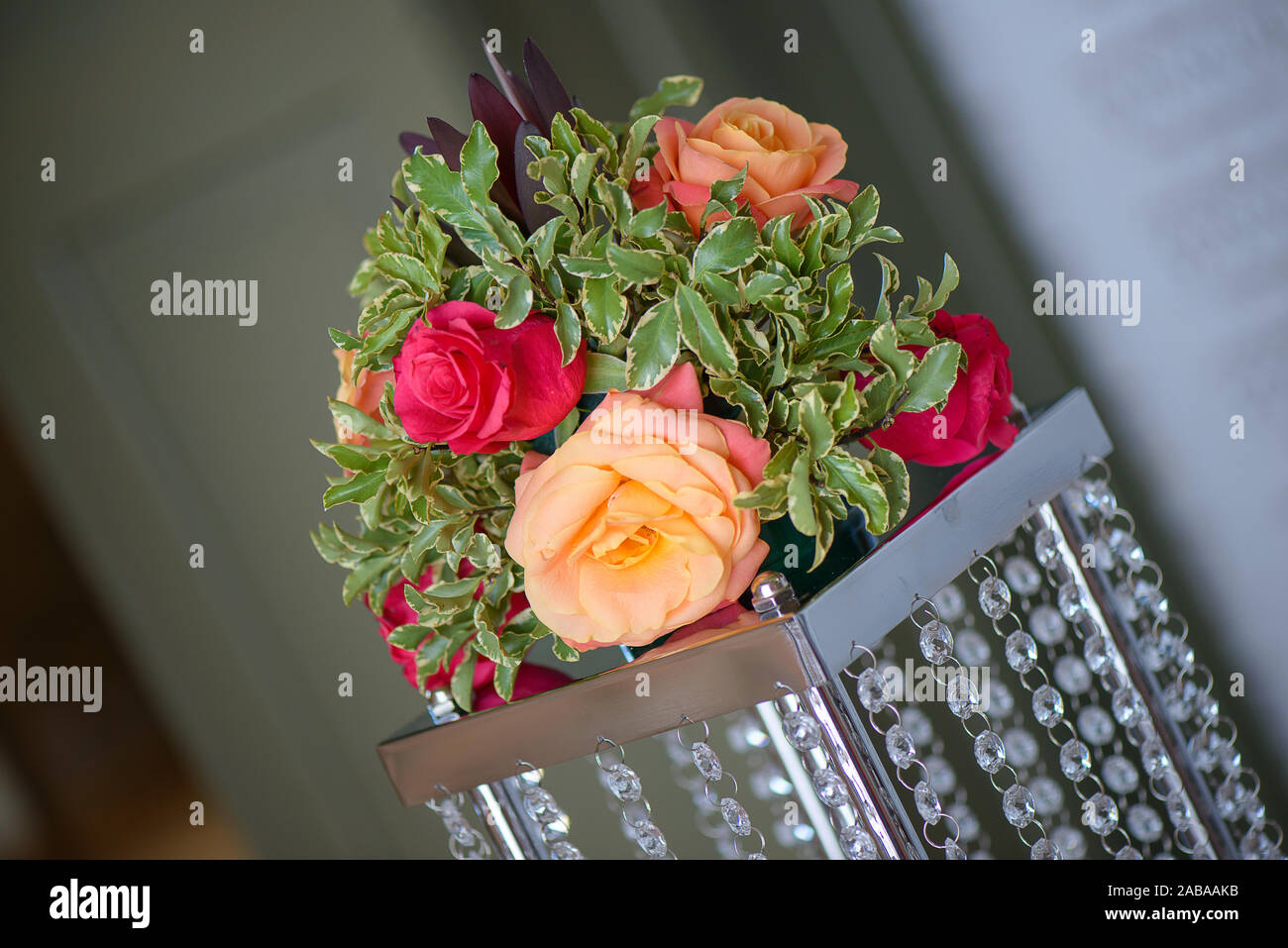Pink and orange roses beautifully arranged in a round delicate bouquet set on a metal and crystals pedestal used as a centerpiece Stock Photo