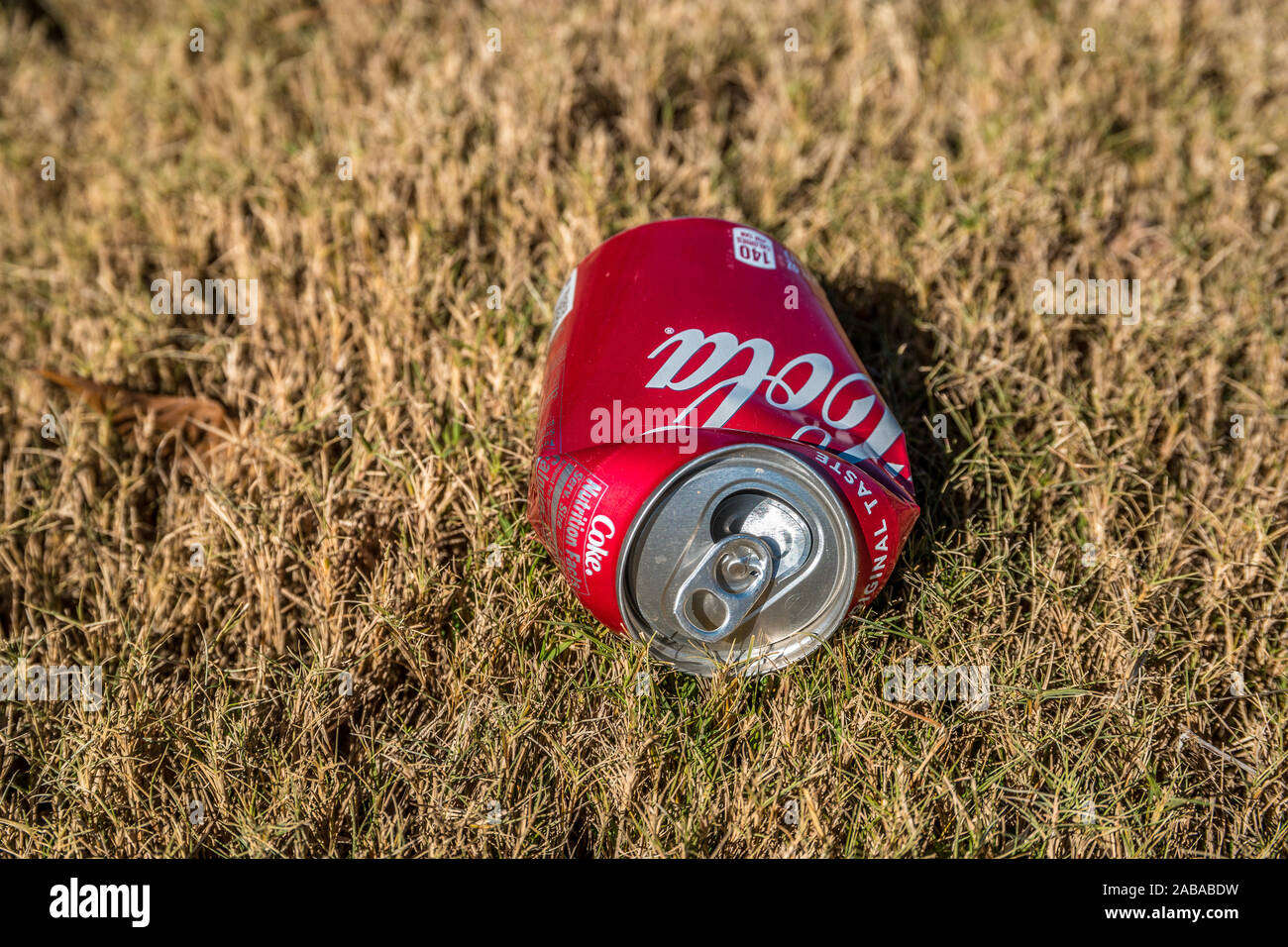 Looking straight on from the top of the crushed Coca-Cola can laying on the grass outdoors empty and discarded on the ground on a sunny day in autumn Stock Photo