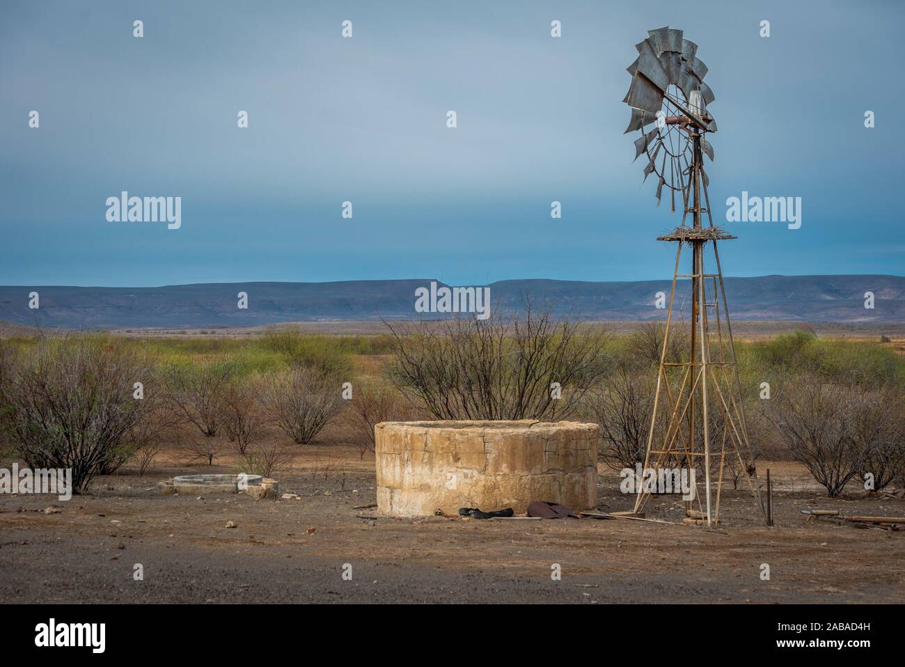 Windmill remains locked in this uncompromising, arrid landscape. The reservoir is dry. The earth is dry. All that grows are hardy Acacia thorn trees. Stock Photo