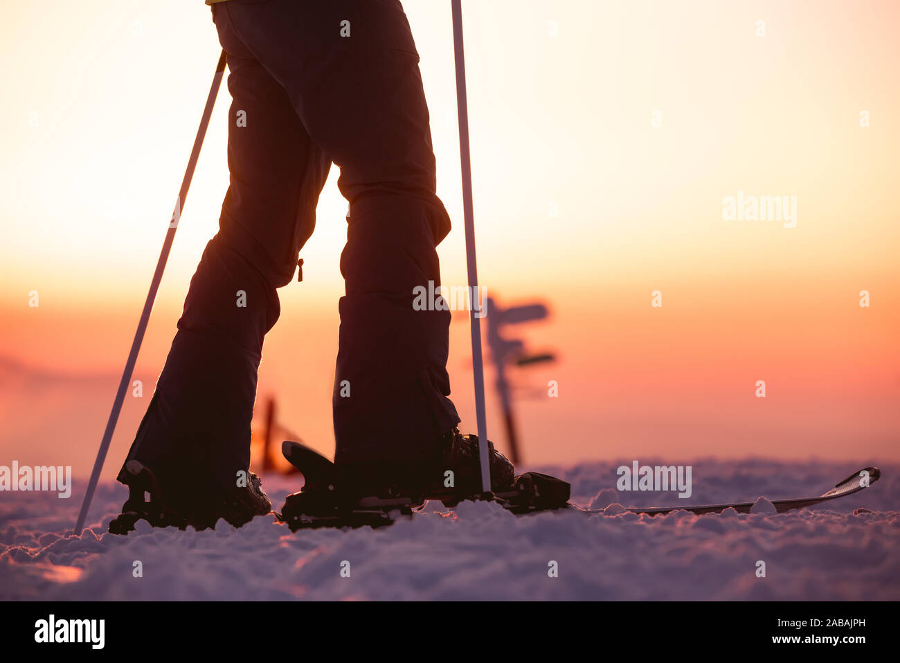 Close Up photo of female skiers legs with ski poles against sunset sky Stock Photo