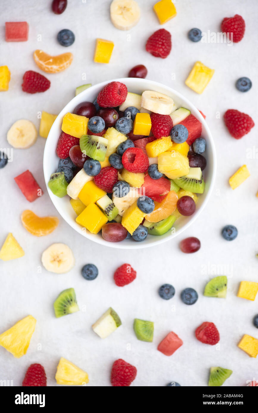 Bowl of cut fruit on a white background. Fruit includes raspberries, blueberries, banana, grapes, mango, pineapple, melon, kiwi and pear Stock Photo