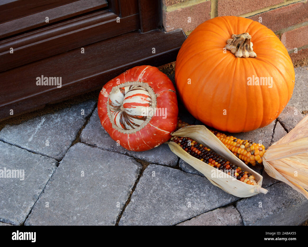 Turks Turban gourd with colourful ornamental corn and large orange pumpkin as Thanksgiving decorations on a stone doorstep with copy space Stock Photo