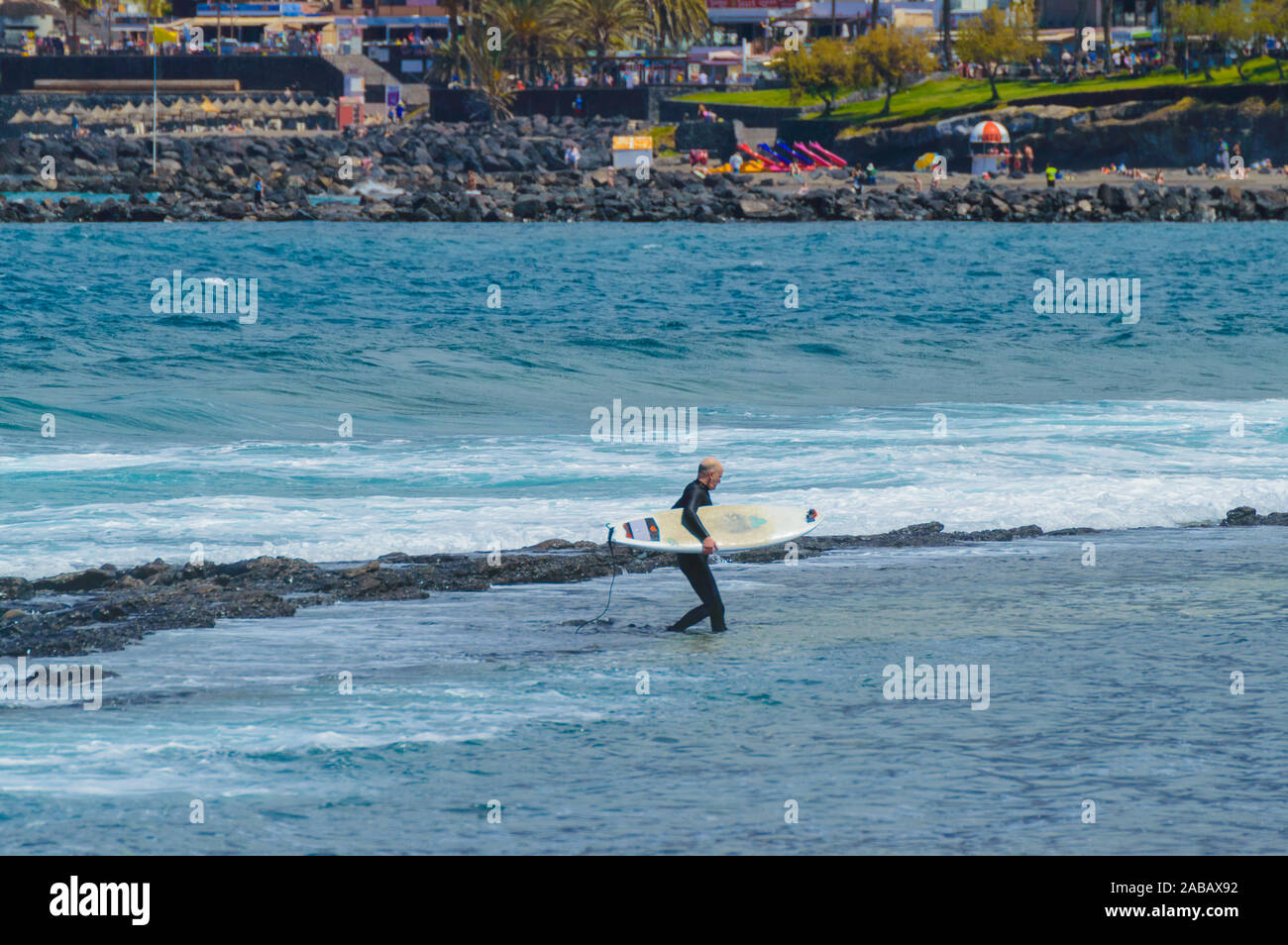 Bald Senior Man Holding A White Table leaving the Atlantic Ocean after enjoying a day of waves on the beach of Las Americas. April 11, 2019. Santa Cru Stock Photo