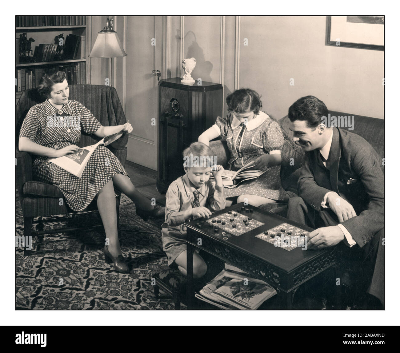 Vintage 1940's Family of four sitting together, reading and playing board games in their sitting room together. 20th Century Black-and-White photograph Post-War Home Life family group From Home Economist 1946 Edition of Living Together in the Family Stock Photo