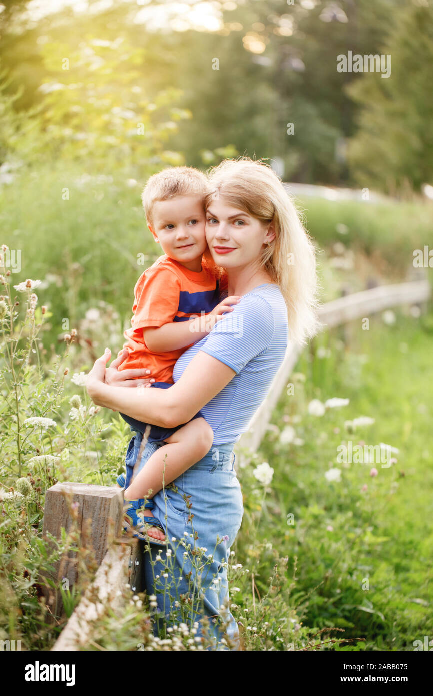 Young blonde Caucasian mother and boy toddler son hugging embracing in park outdoor on summer day. Mom and child love and tenderness. Happy family chi Stock Photo