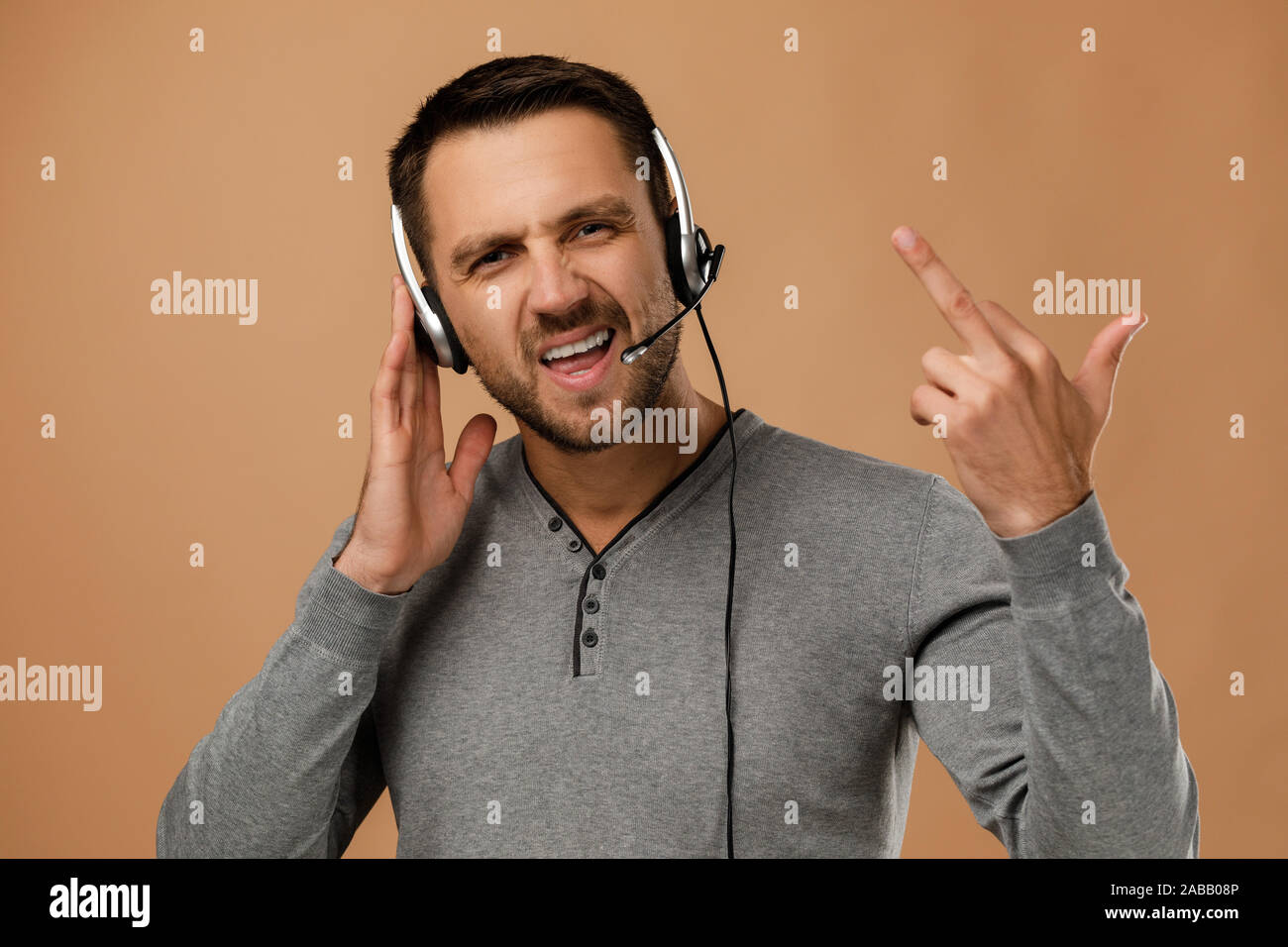 indignant unrestrained call center worker man isolated on beige background. Young angry employee telesales agent using headset. Stock Photo