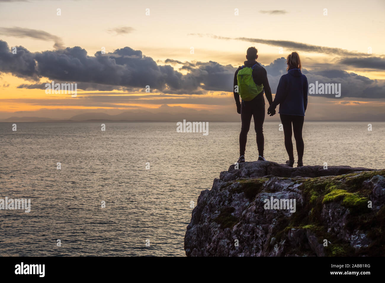 Adventurous couple holding hands and standing on a rocky cliff by the ...