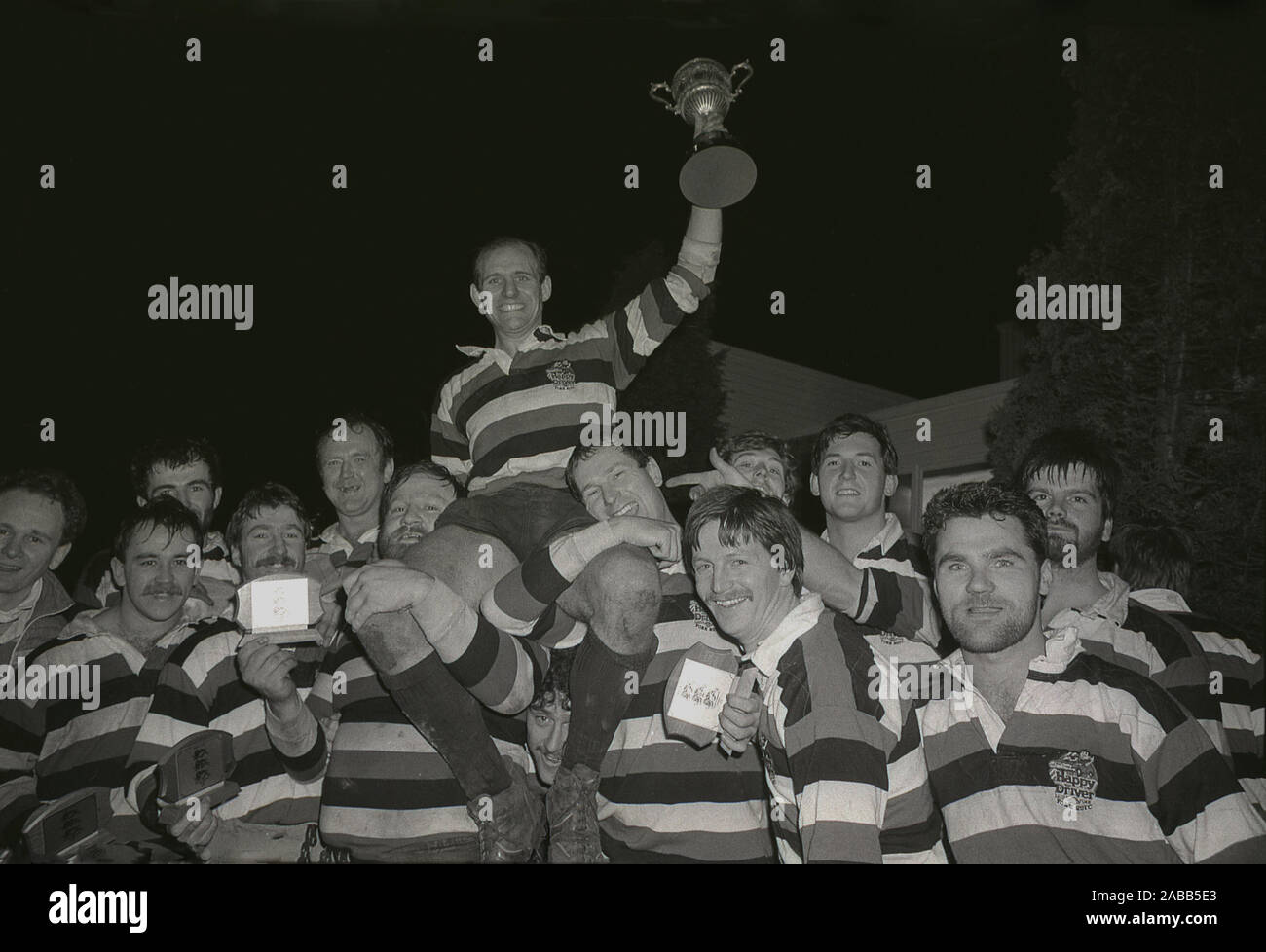 1980s, historical, winning captain holding the trophy being aloft by members of his team, after playing a night-time game of rugby union, England, UK. Stock Photo