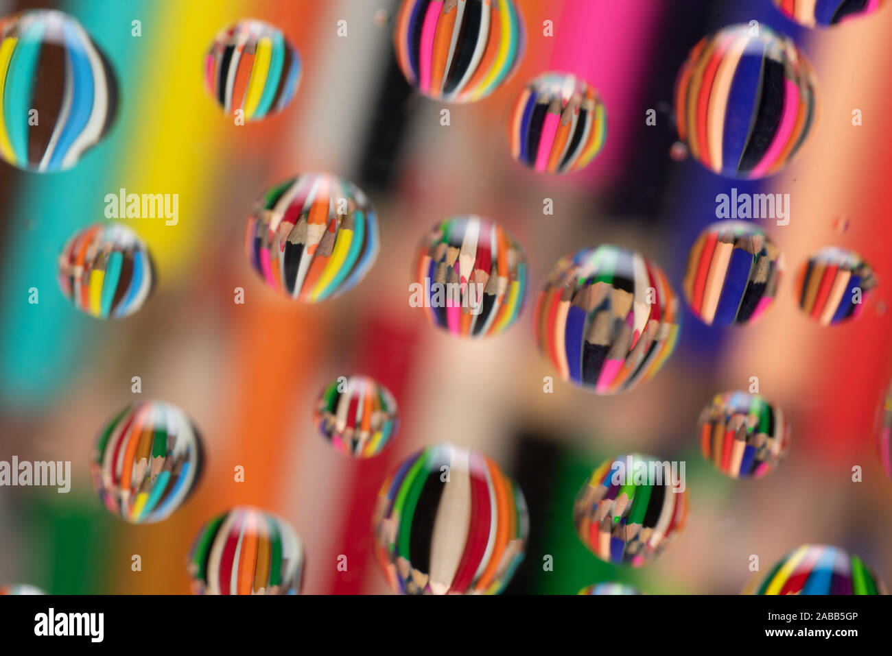 Coloured drawing pencils reflected on waterdrops resting a piece of glass creating a wonderful colourful background. Stock Photo