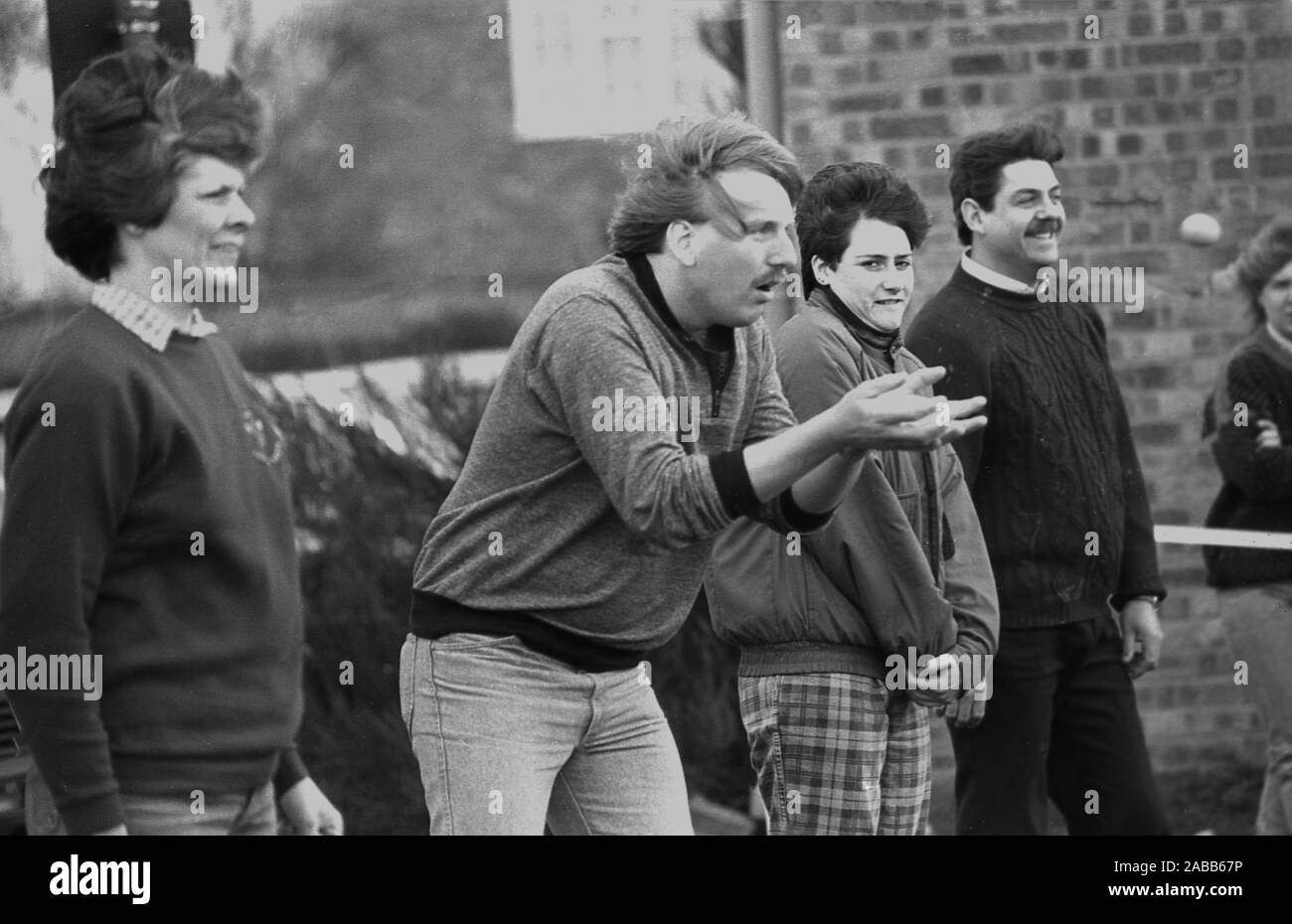1980s, historical, outside spectators stand near a man taking part in a traditional egg throwing competition, attempting to catch the delicate egg which is in mid-air coming towards him, England, UK.  Egg throwing is a two person sport requiring distance lobbing and the ability to catch. Each team member begins by standing ten metres apart, spreading out after each successful catch. But....drop or break the egg and you are out! It is believed that egg throwing first occurred in the 1300s, gradually becoming an informal sport called the 'egg toss', played at country fairs and fetes. Stock Photo