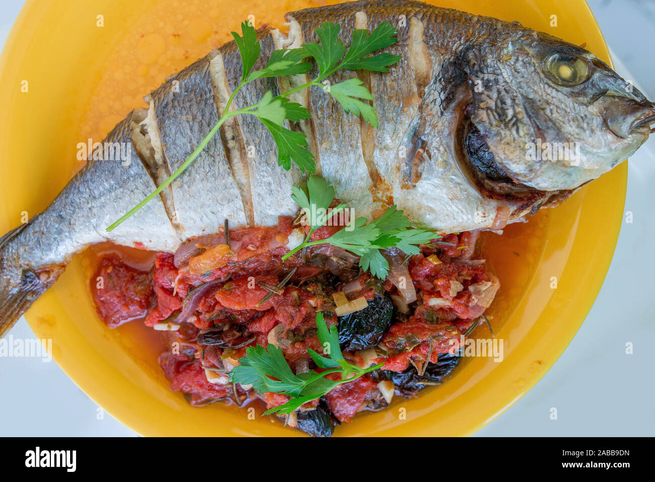Cooked whole sea bream fish with tomato and parsley garnish beautifully served on a plate. Stock Photo