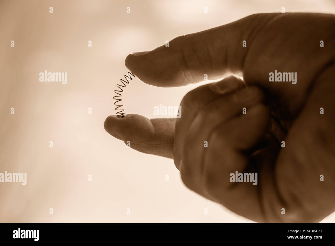 Caucasian hand compressing a metal spring between a thumb and finger ...
