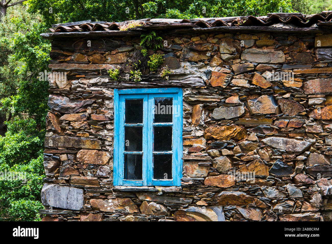 Close up of a window with blue trim and a rustic stone wall in the village of Cerdeira, Portugal Stock Photo