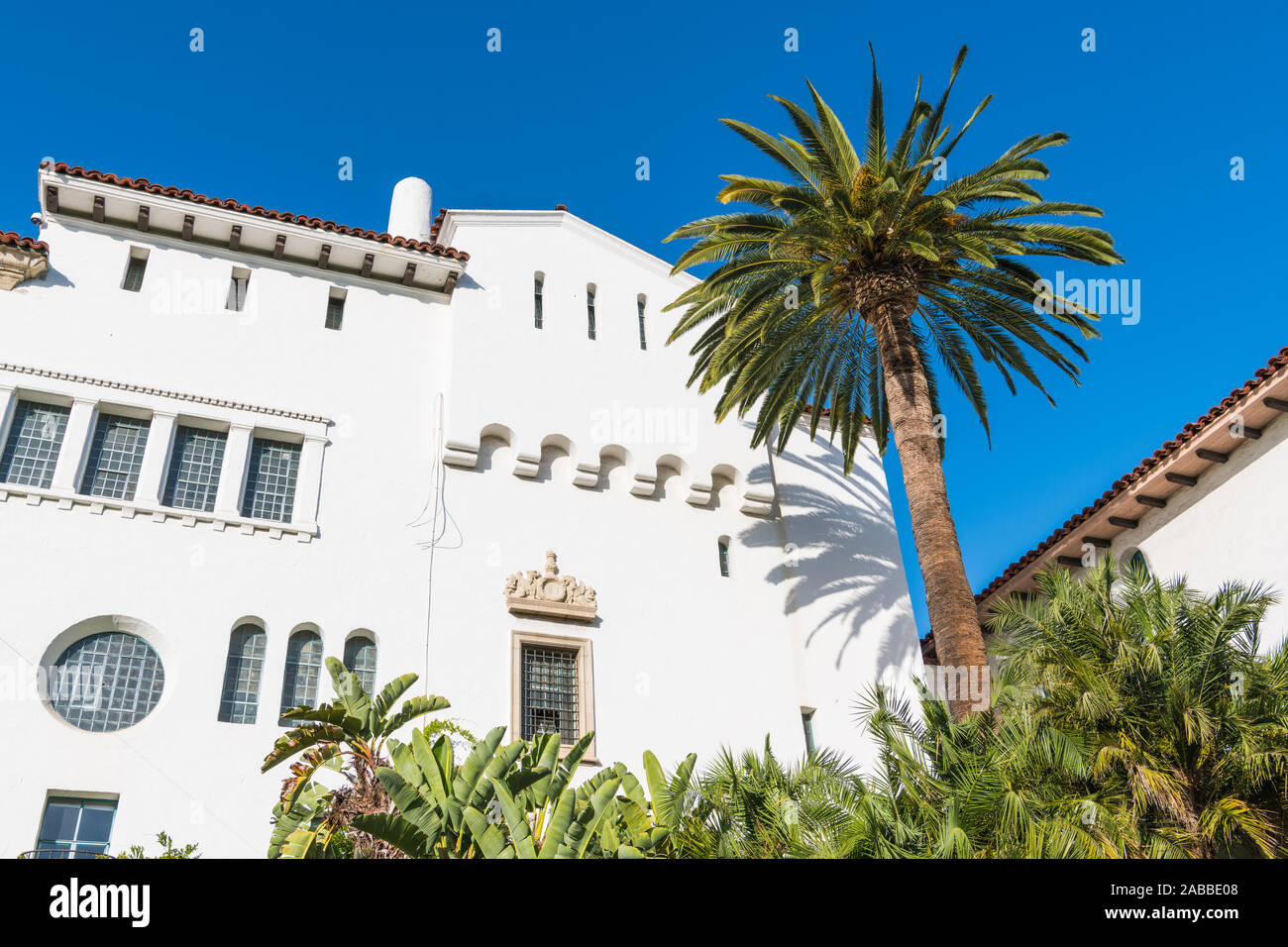 A palm tree and a historic white Spanish colonial revival architecture style building with ornate windows and trim in Santa Barbara, California, USA Stock Photo