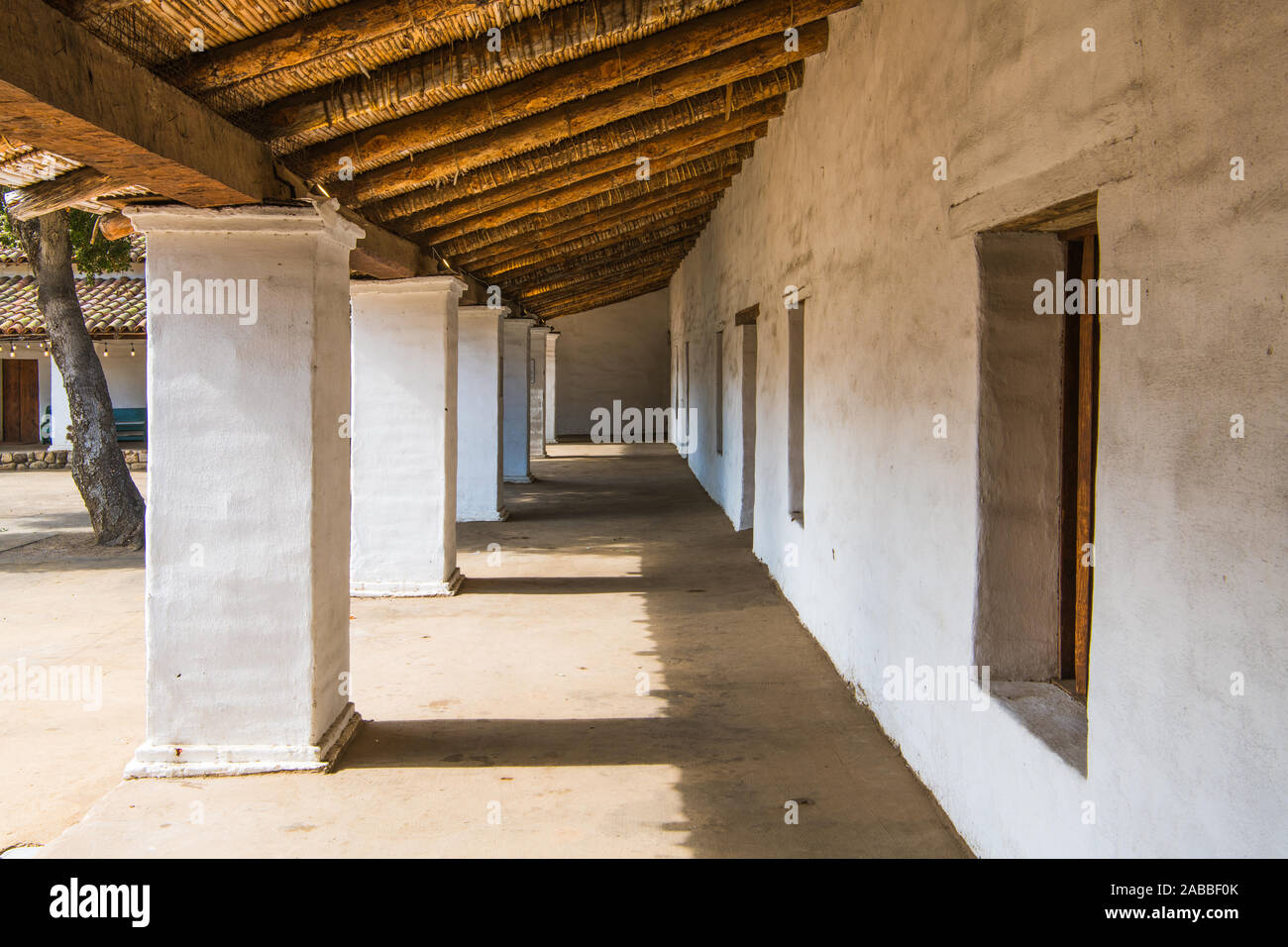 Long exterior corridor with white plastered columns and walls under the rustic wooden roof of an historic Spanish style building in Santa Barbara, Cal Stock Photo