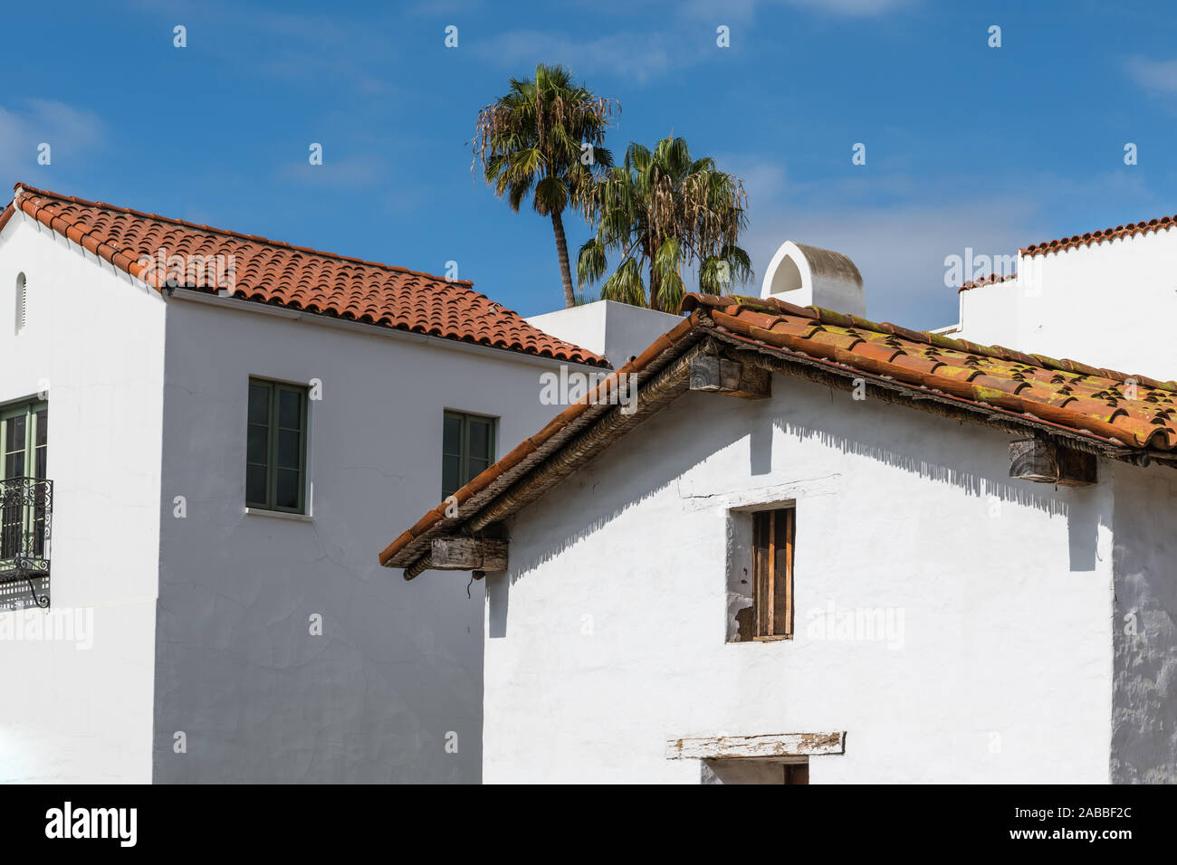 New and old Spanish style buildings with white plaster walls and red tile roofs under a blue sky with palm trees in downtown Santa Barbara, California Stock Photo