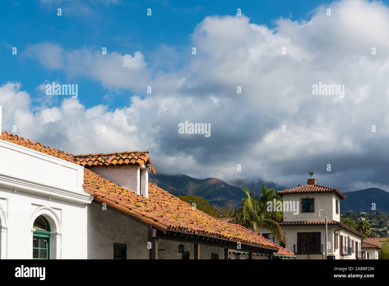 Typical scene of Spanish Colonial Revival architecture buidlings with white plaster walls and red tile roofs under palm trees, mountains, and white fl Stock Photo