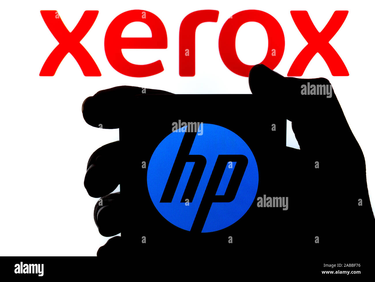 The silhouette of smartphone with HP logo hold in a hand and XEROX logo on the blurred background. Concept for takeover bid. Real photo,no alterations Stock Photo