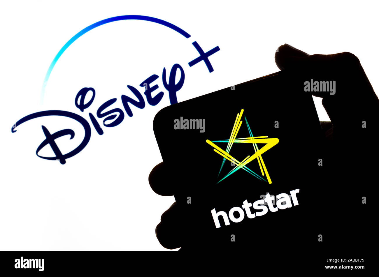 Hotstar logo on the silhouette of a smartphone hold in hand and Disney+ logo at the background. Concept. Real photo, not a montage. Stock Photo