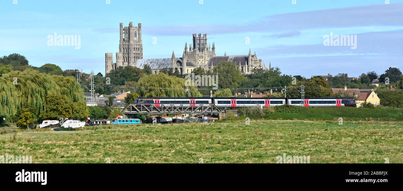 Ely Cathedral beyond train departing Ely Station Cambridgeshire boats on River Great Ouse below railway bridge  East Anglia Fens landscape England UK Stock Photo