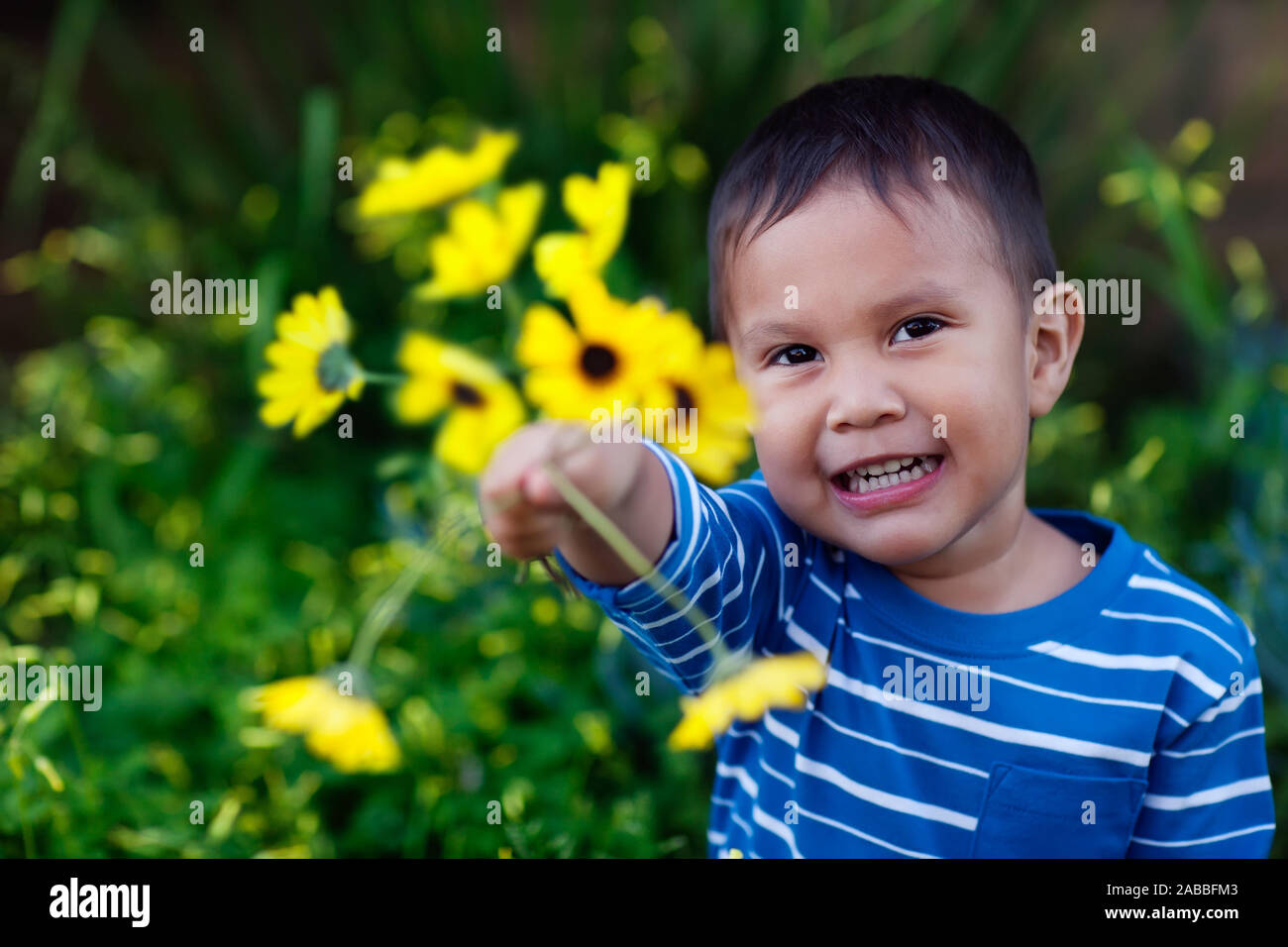 Smiling young son giving an arrangement of yellow flowers he is holding to show affection and love. Stock Photo