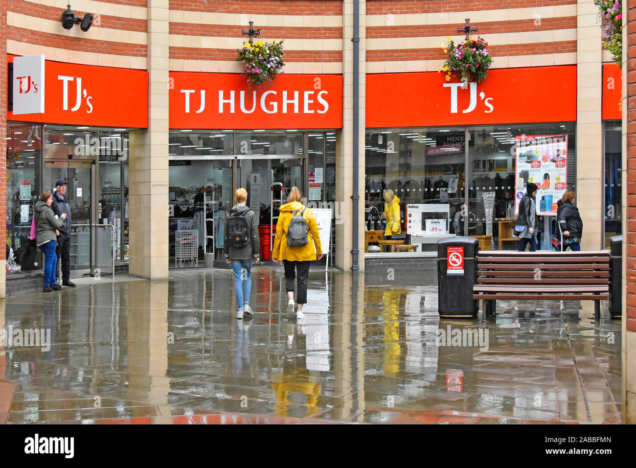 Wet weather street scene & pavement reflections rain falling on shoppers walking to TJ Hughes retail shop business in Durham County Durham England UK Stock Photo