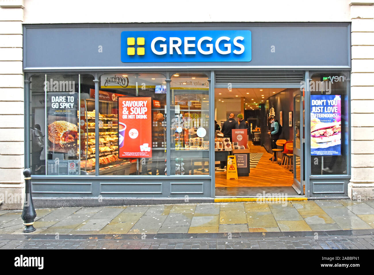 Shop front & interior Greggs sandwiches pies pastries & bakery food store customers & tables indoors out of wet rainy exterior in Durham England UK Stock Photo