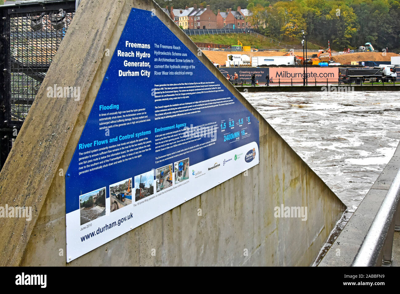 Side wall hydro electricity power generator installation information panel & River Wear fast water flow during potential flood risk Durham England UK Stock Photo