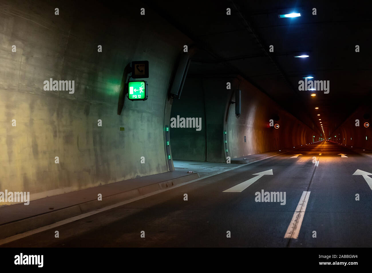 Automobile auto dark car tunnel with white arrows on asphalt showing way direction. Emergency exit sign with many lights. Empty underground vehicle Stock Photo