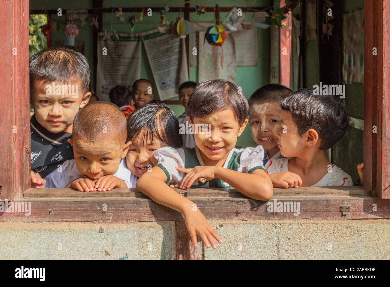 Elementary school students lean out of their classroom window with smiles and curiosity in Kanne village on the Chindwin River of Myanmar (Burma) Stock Photo