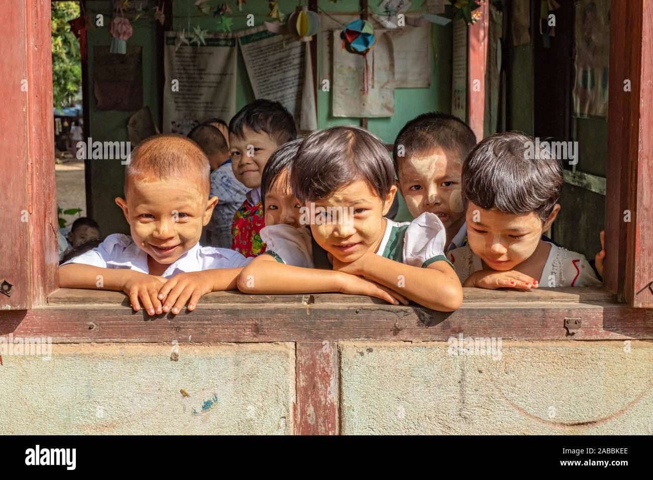 Elementary school students lean out of their classroom window with smiles and curiosity in Kanne village on the Chindwin River of Myanmar (Burma) Stock Photo