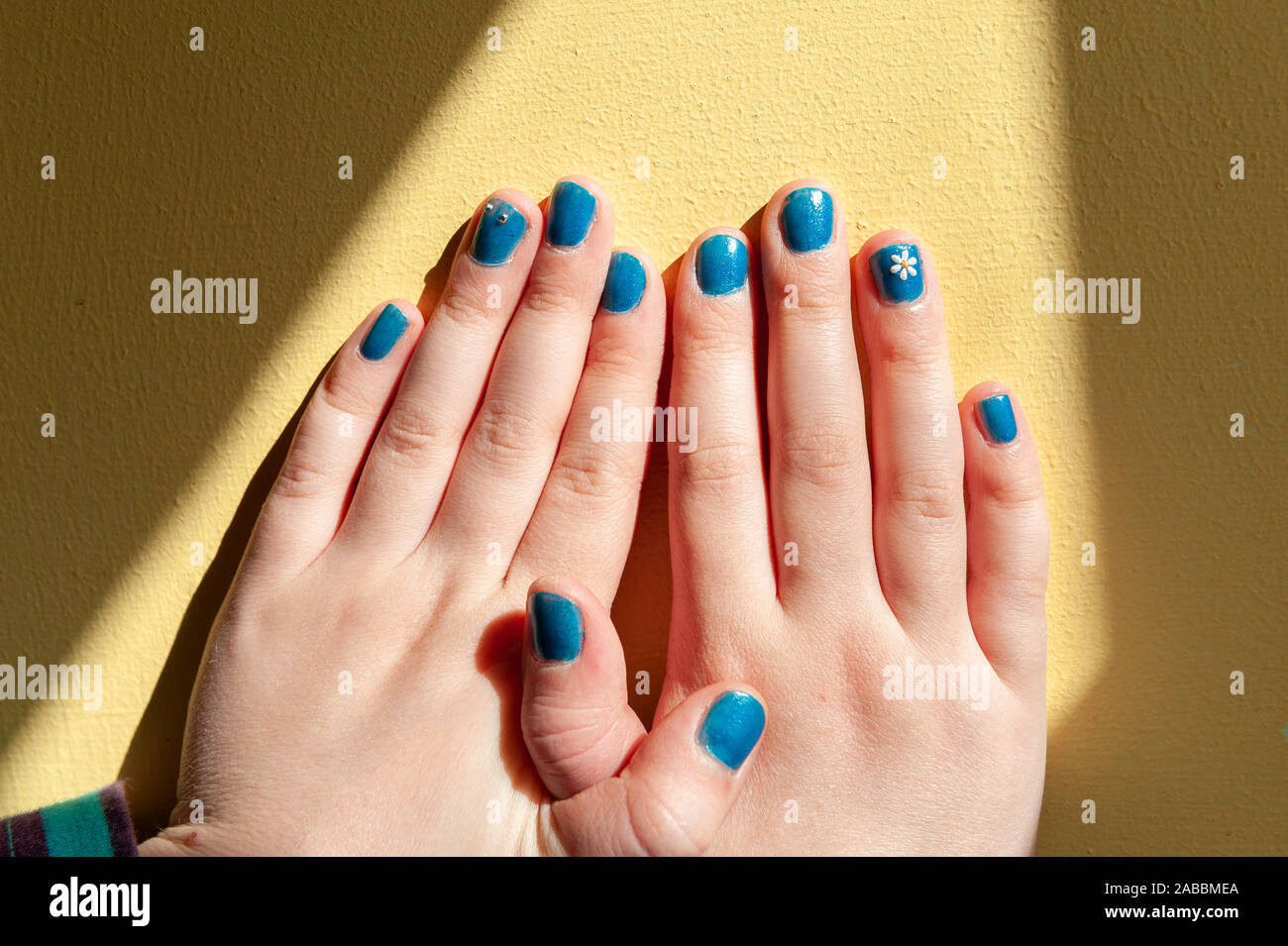 Vibrantly painted blue fingernails in a line with interlocking thumbs