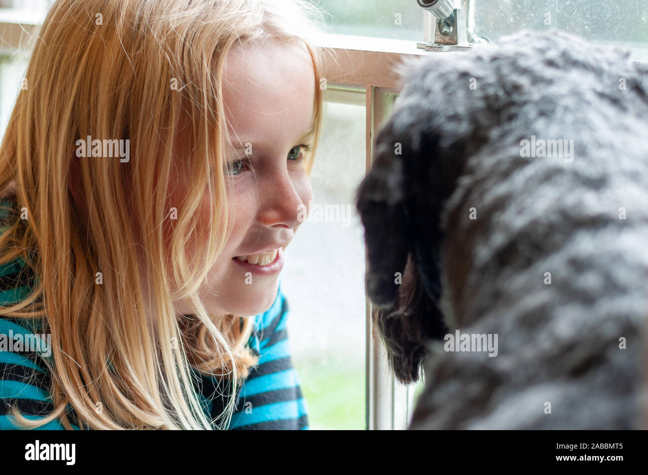 Pretty Blonde Girl Happily Gazing At Her Black Dog In Front Of A