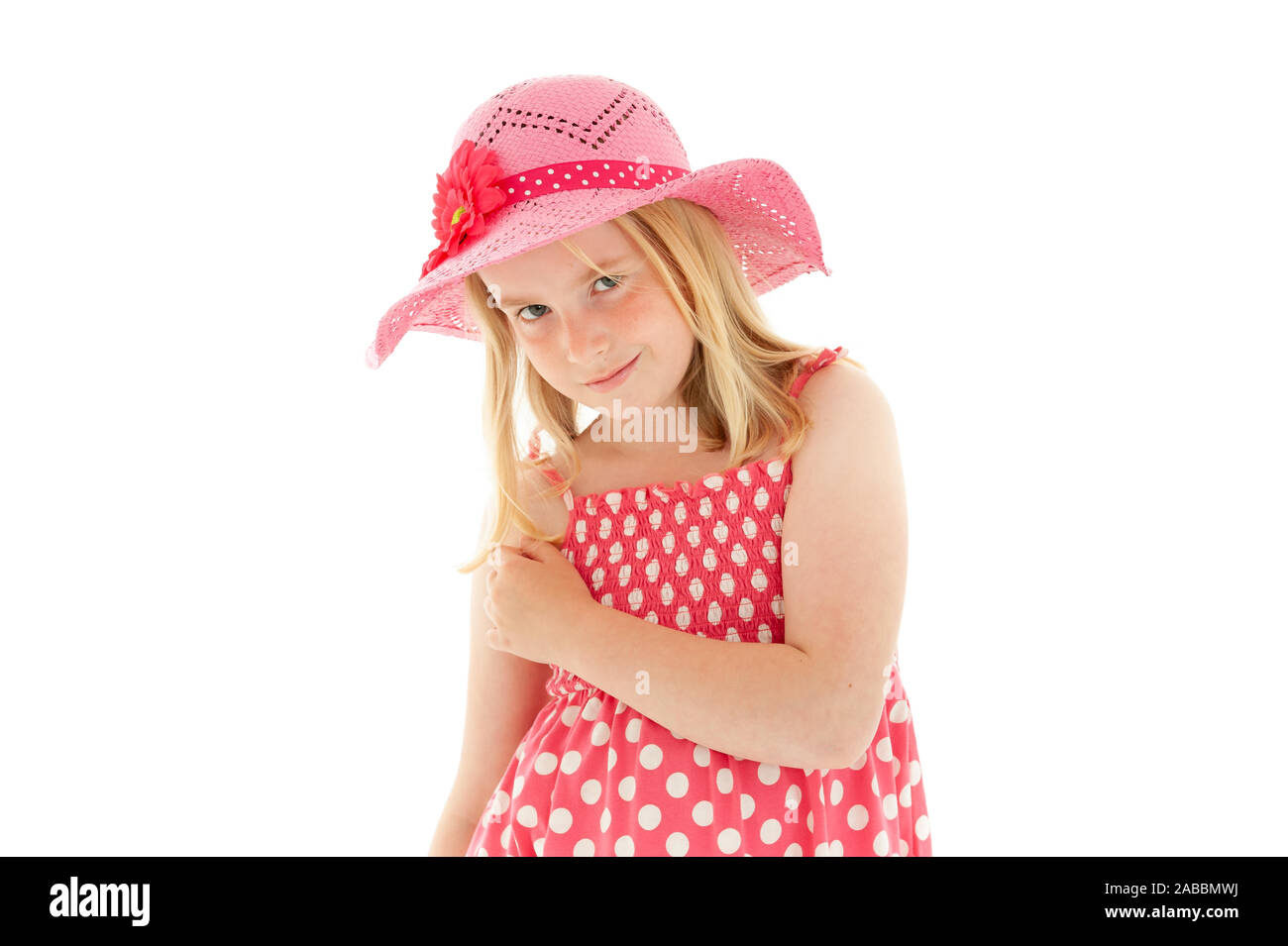 Beautiful young blonde girl with enigmatic smile wearing big pink floppy hat and a polka dot dress. Isolated on white studio background Stock Photo