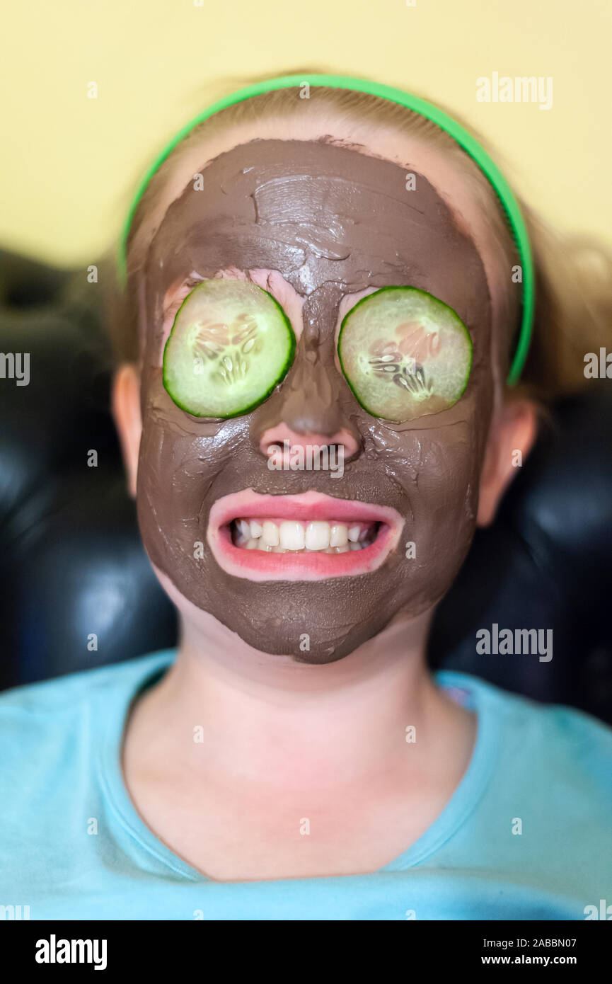 Happy young girl with a face pack on and cucumber slices on her eyes Stock Photo