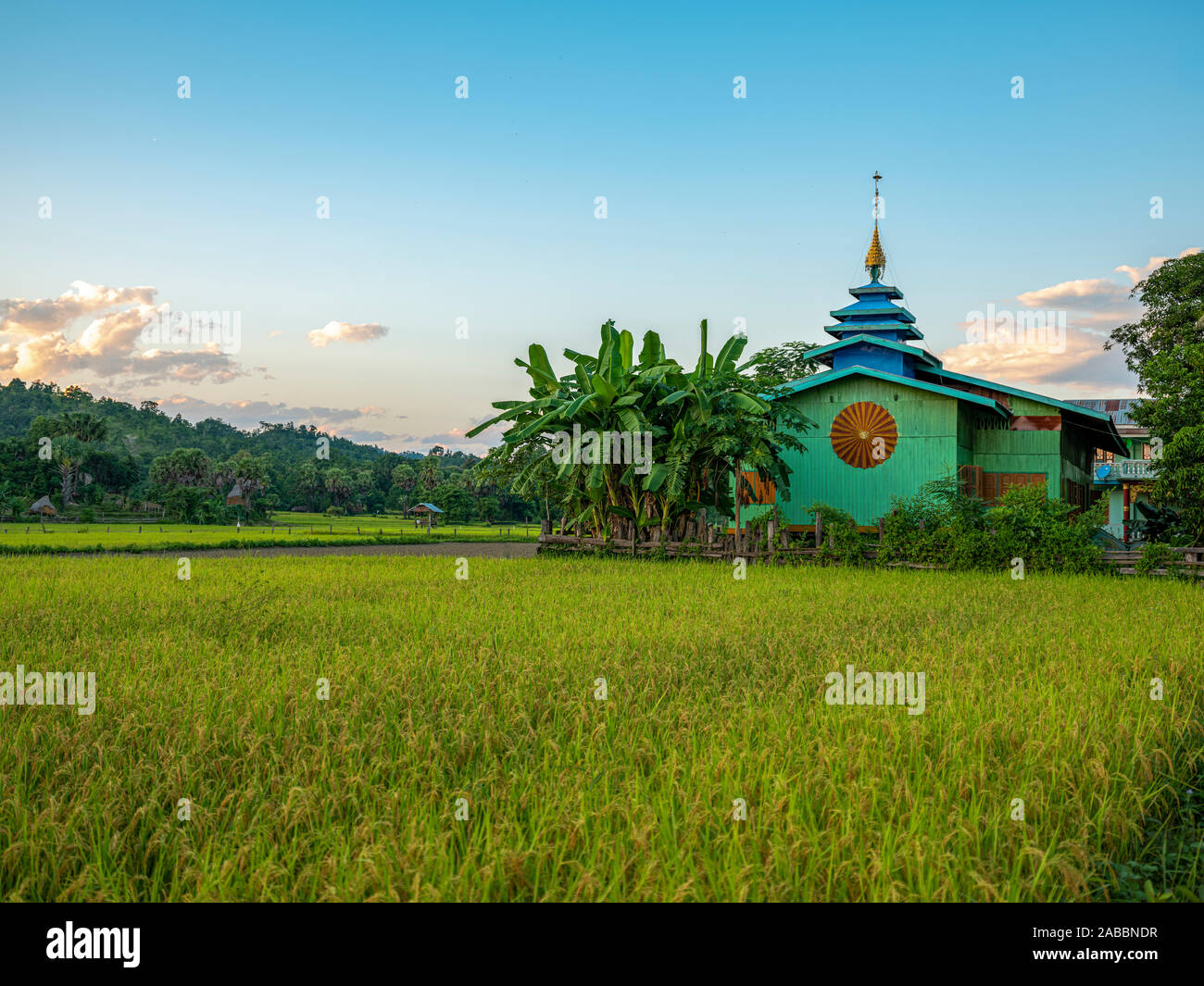 Colorful Buddhist monastery painted in blue and turqoise with pagoda roof amidst rice fields in the Chindwin River village of KoneGyi, Myanmar (Burma) Stock Photo