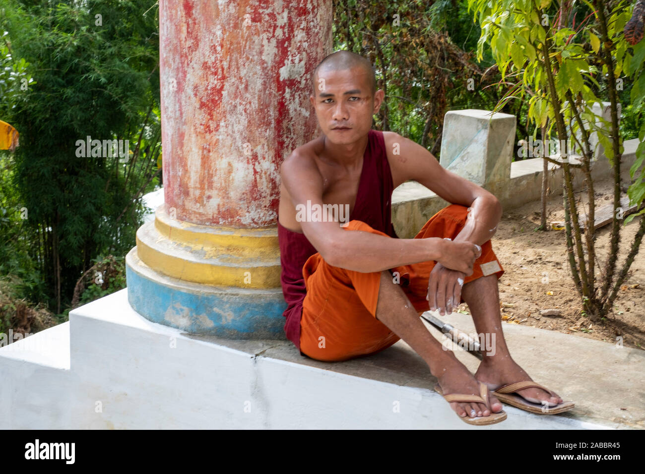 A young Buddhist monk with shaved head dressed in orange and red garb