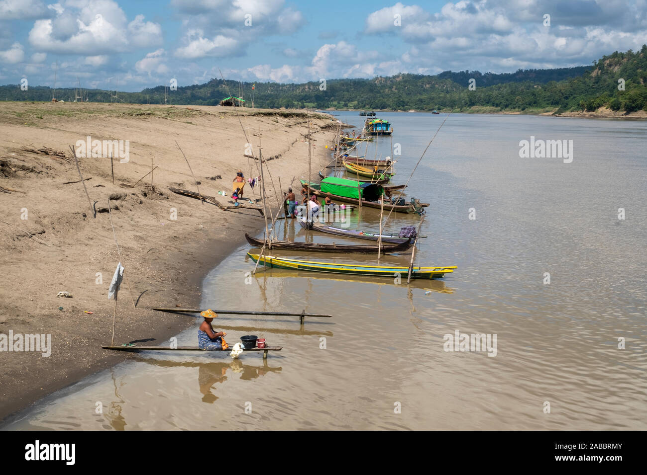 Small boats line the shoreline of the Chindwin River in northeastern Myanmar (Burma) while local residents wash their laundry in the river. Stock Photo