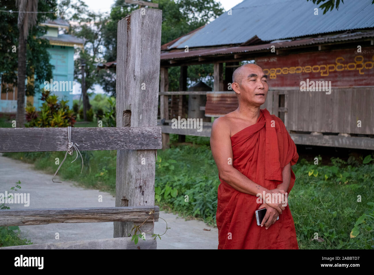 An older Buddhist monk in a scarlet robe stands in front of his monastery in a rural village along the Chindwin River in northwestern Myanmar (Burma) Stock Photo