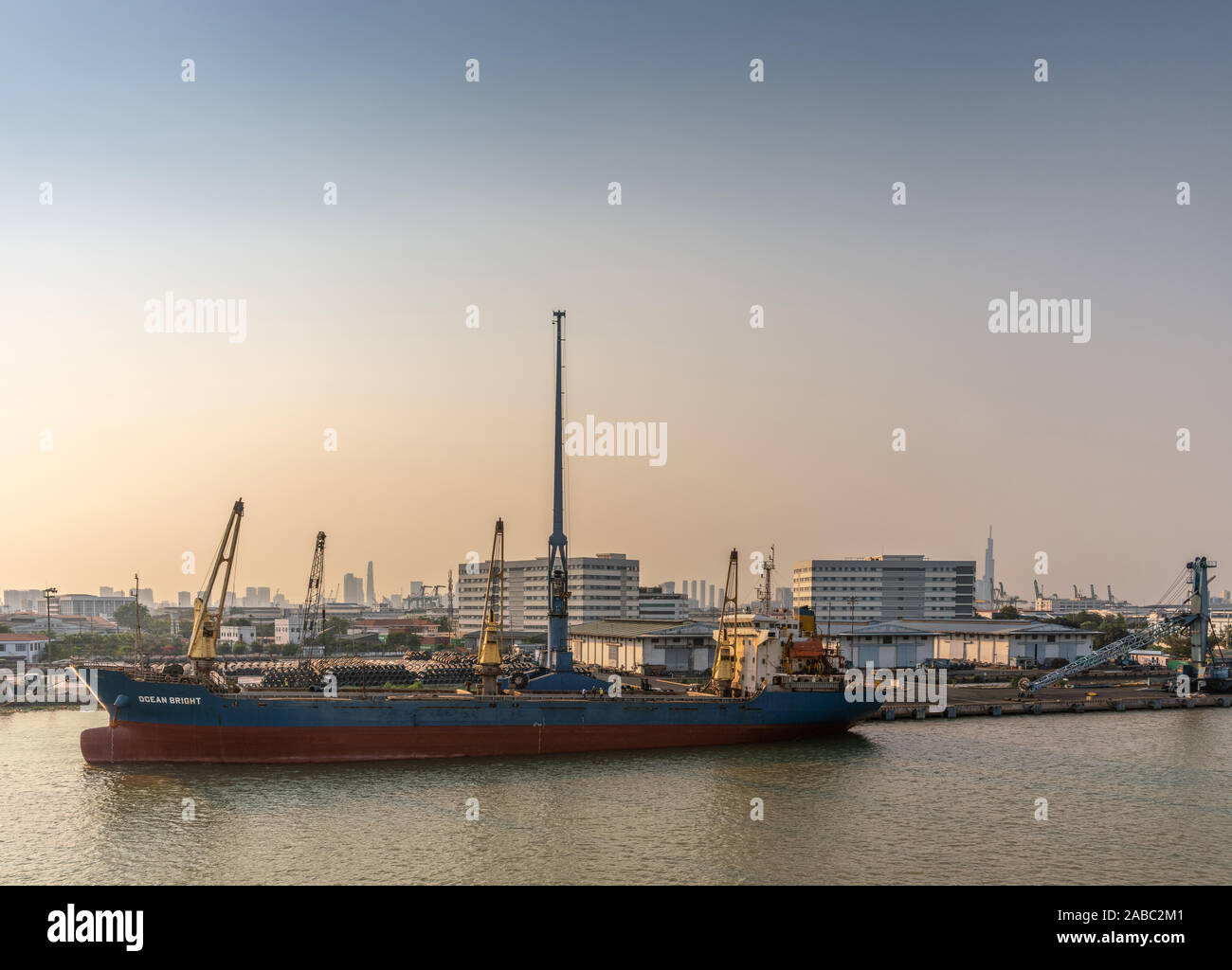 Ho Chi Minh City, Vietnam - March 13, 2019: Song Sai Gon river at sunset. Blue-red Ocean Bright sea cargo vessel docked and worked on by tall blue cra Stock Photo