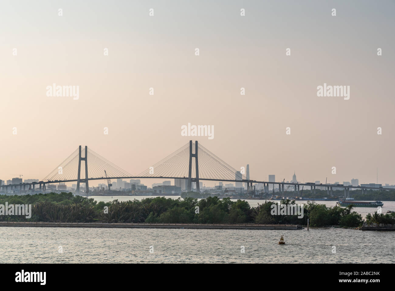 Ho Chi Minh City, Vietnam - March 13, 2019: Song Sai Gon river at sunset. Phu My suspension bridge with green belt and river water in front and tall d Stock Photo