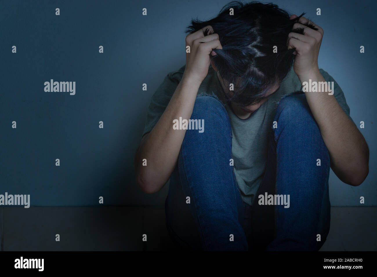 sad man hug his knee and cry sitting alone in a dark room. Depression ...