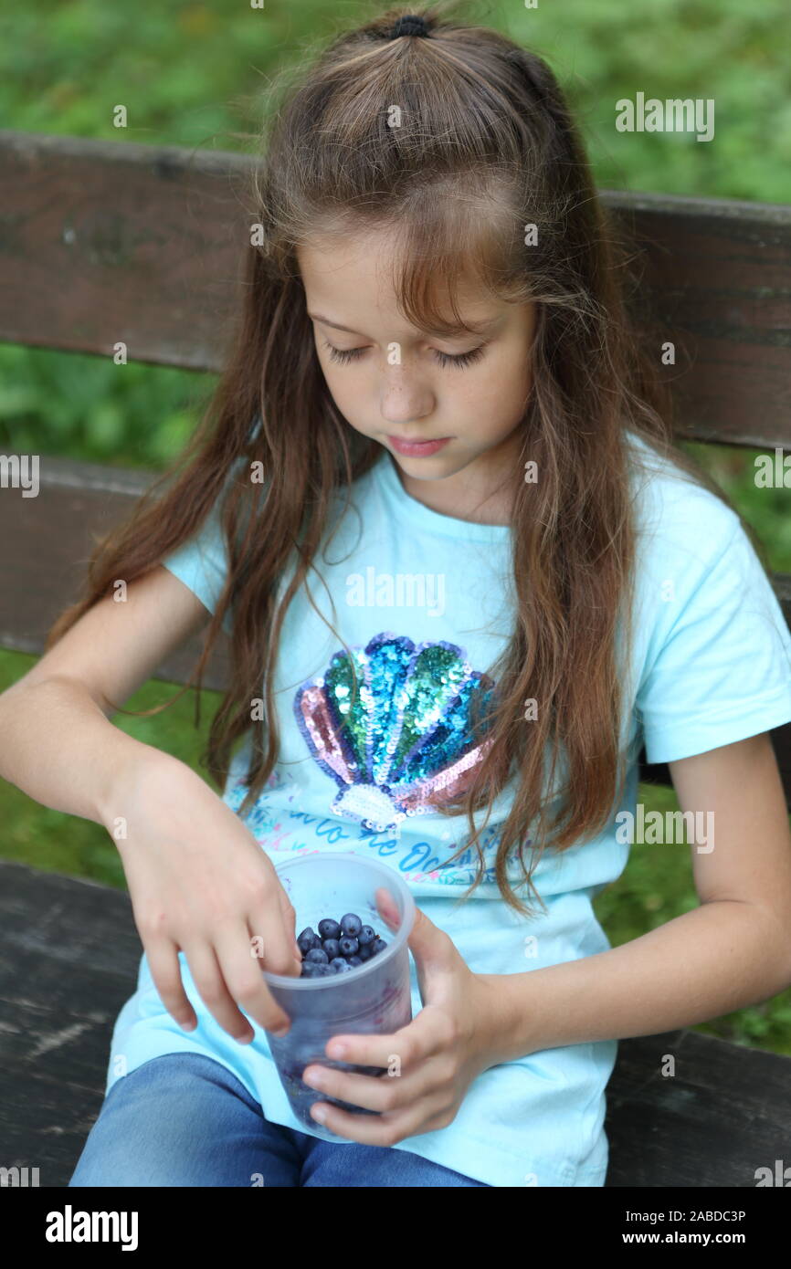 Little girl sits on a bench and eats blueberries Stock Photo - Alamy