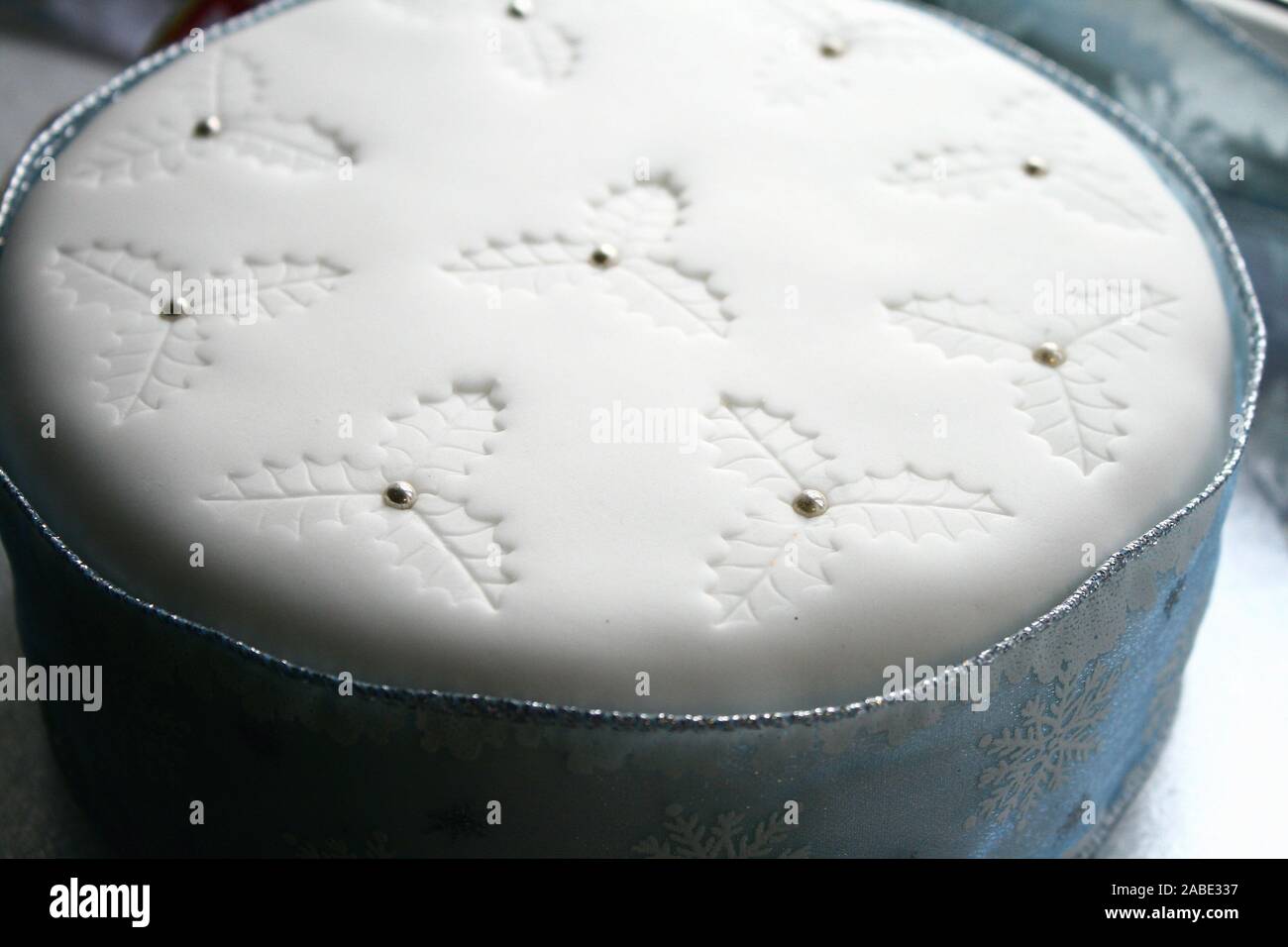 Elegant Blue and white Christmas fruit cake, white icing on top and holy impressions with silver balls, snowflake ribbon all around the cake, blue and Stock Photo