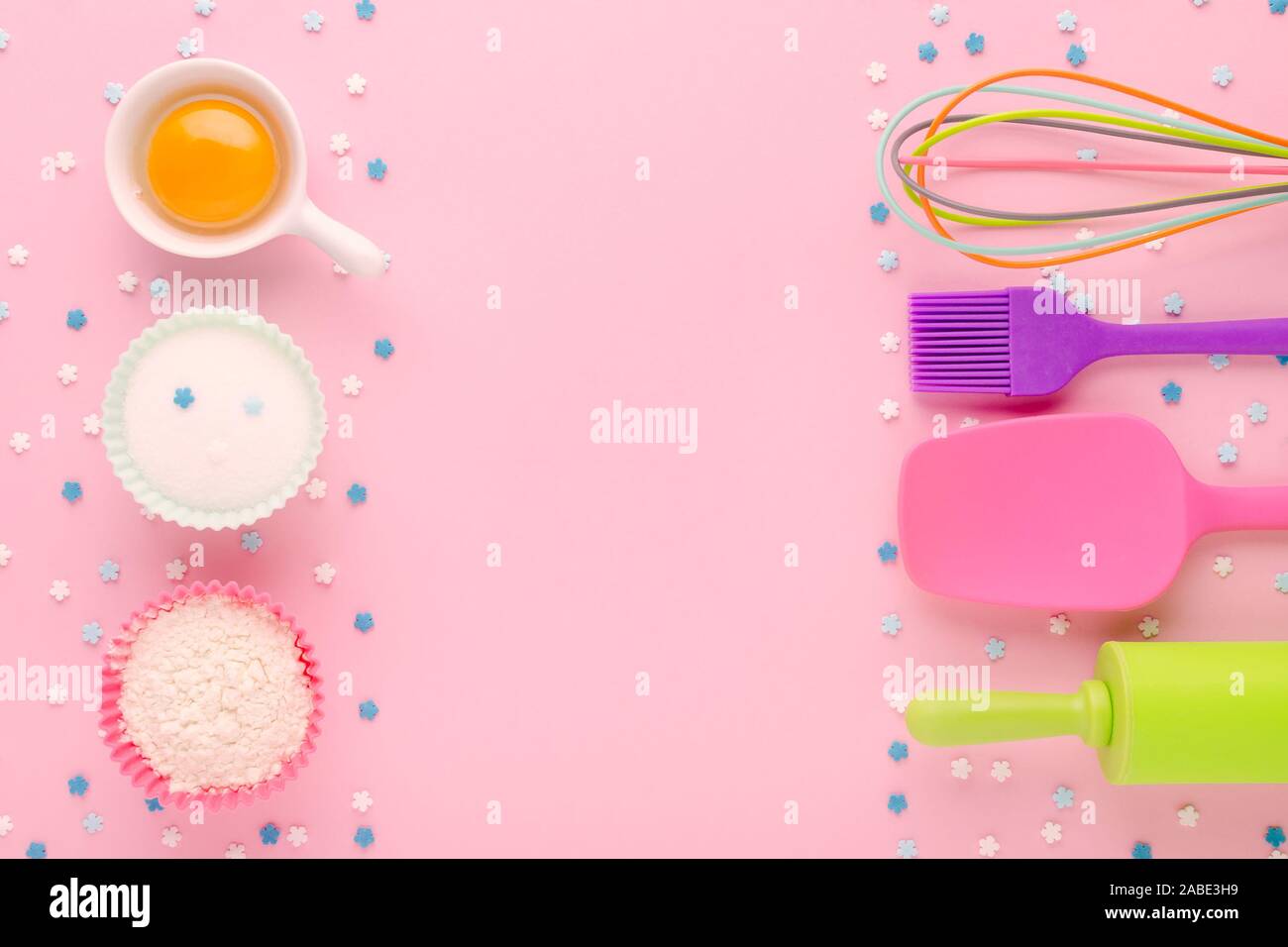 baking ingredients, egg, flour, sugar, sweet decoration and kitchen tools on pink background with copy space Stock Photo