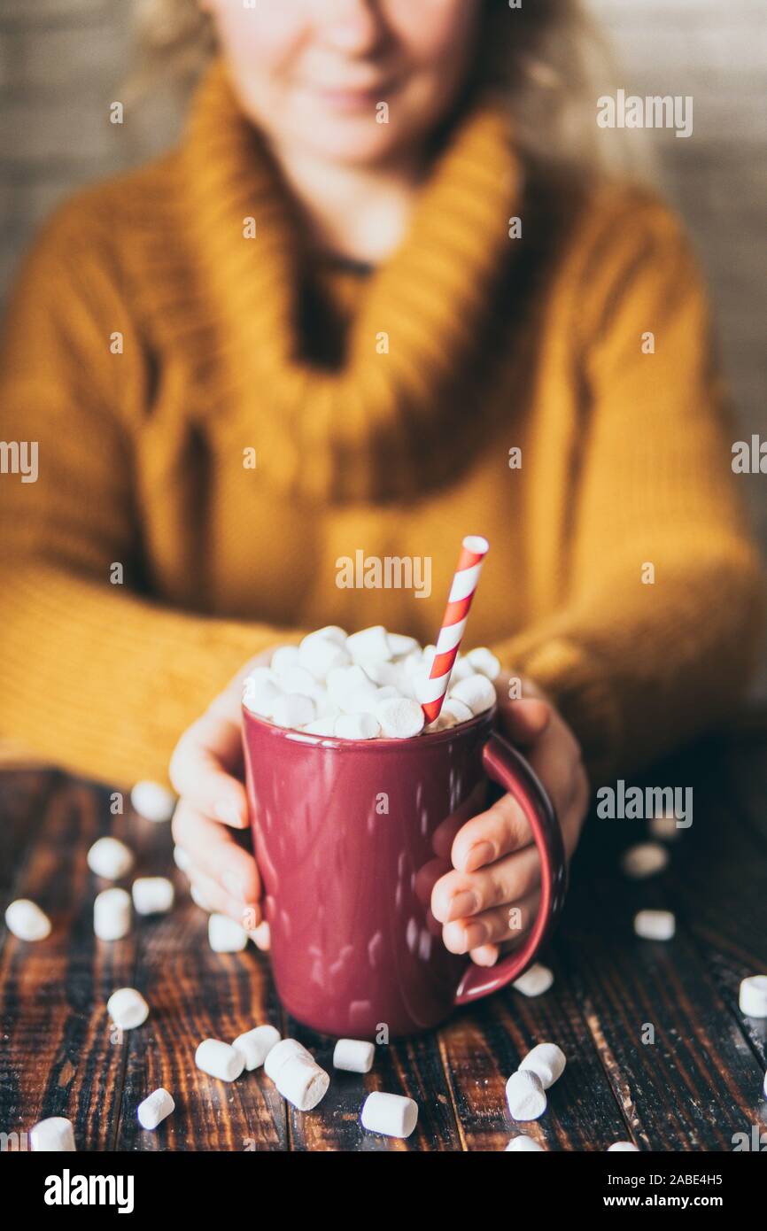 Woman in yellow sweater holding hot chocolate mug covered with marshmallow on dark wood background. Vertical orientation Stock Photo