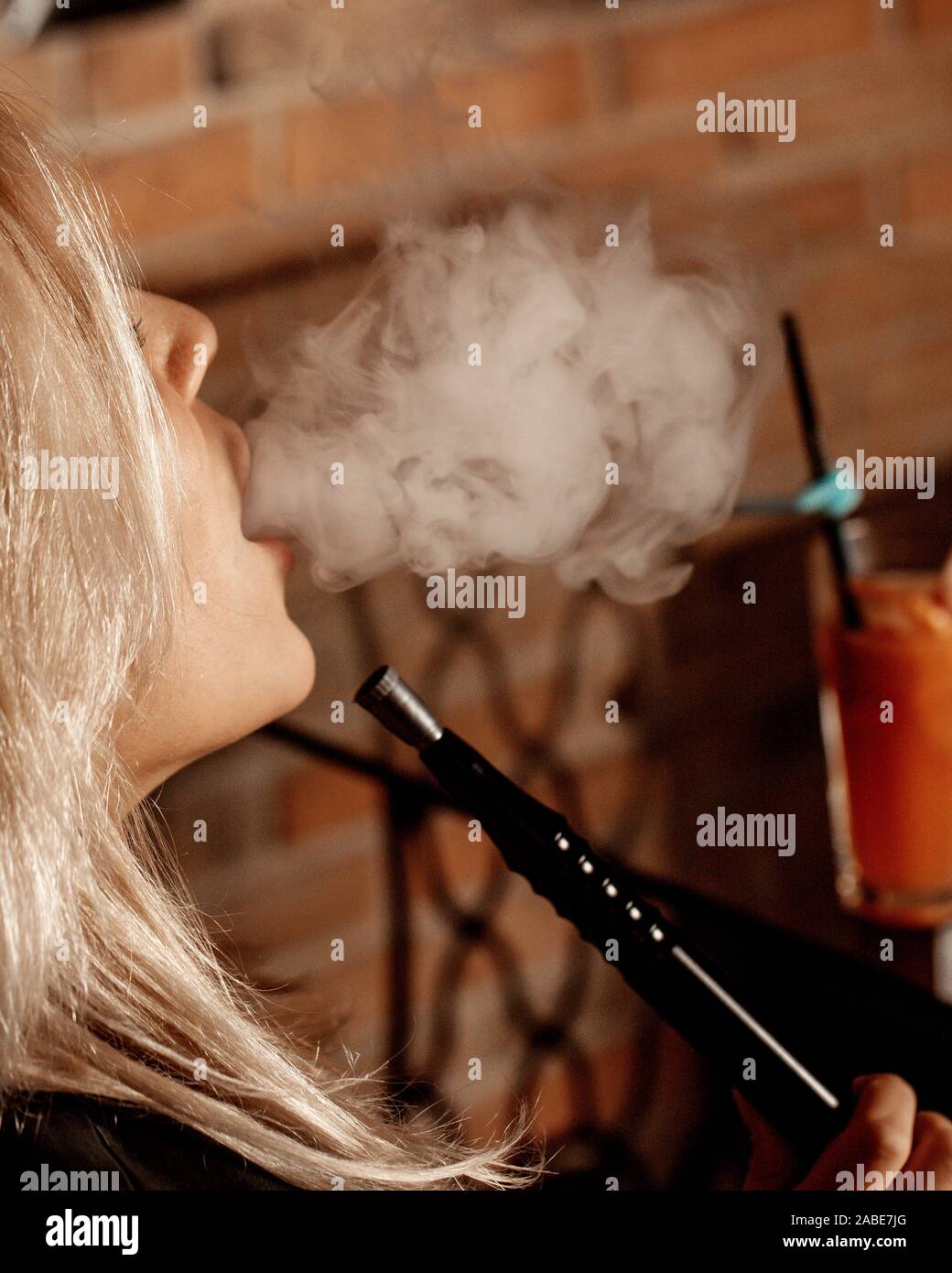 woman smoking hookah and blowing smoke at the restaurant Stock Photo
